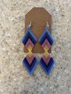 Native American-made beaded large double diamond shaped earrings in chevron design of blues, purple, pinks and yellow. Measures 3" long x 1" wide, stainless steel hooks with rubber backings. Multicolor Beaded Geometric Earrings, Handmade Blue Geometric Earrings, Blue Bohemian Jewelry With Geometric Shape, Handmade Blue Geometric Jewelry, Bohemian Blue Geometric Earrings, Blue Bohemian Geometric Jewelry, Bohemian Blue Geometric Jewelry, Native Earrings, Earrings Patterns