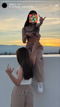 two women are sitting on a wall and one is holding up her cell phone to take a photo