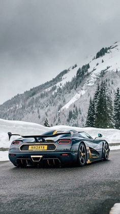 a blue sports car driving down the road in front of a snowy mountain covered with trees