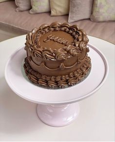 a chocolate cake sitting on top of a white plate next to a couch and pillows