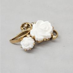 This is part of Chairish’s Costume Jewelry assortment.  1960s goldtone white molded resin roses with clear round rhinestone accents brooch with security clasp. Marked "KRAMER." Measures: 2 1/16 inches long by 1 1/4 inches wide. Condition: Good; some goldtone wear to high points and back, glue residue on back.  Kramer was a costume jewelry maker based out of New York. During the 1950s it created jewelry for Christian Dior. Costume Jewelry Makers, Resin Rose, Rhinestone Brooches, Jewelry Maker, Clear Rhinestones, Vintage 1960s, Costume Jewelry, Christian Dior, Glue