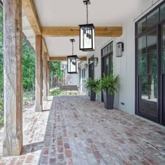 a porch with brick floors and lanterns hanging from it's ceiling, along with potted plants on either side