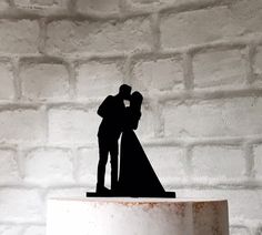 a wedding cake topper that has a bride and groom silhouette on it, against a brick wall