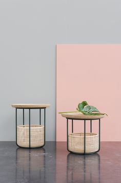 two round tables with plants on them in front of a pink wall