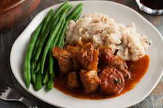 a white plate topped with meat and mashed potatoes next to green beans on a table