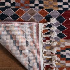 an area rug with various colors and fringes on top of wooden floor next to wall