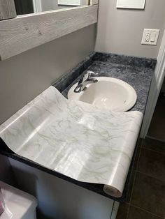 a white sink sitting under a bathroom mirror next to a counter with a roll of toilet paper on it