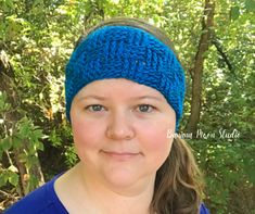 a woman wearing a blue knitted headband in front of some trees and bushes