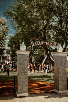 people are walking around in the park near two large stone pillars that say happy halloween