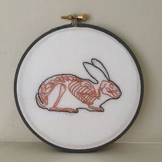 a white wall hanging with an orange and black embroidered rabbit on it's side