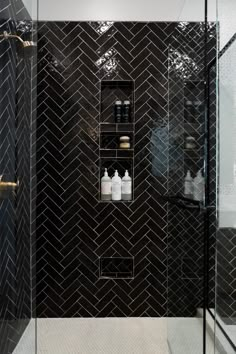 a black and white tiled shower with shelves on the wall, toiletries in the corner