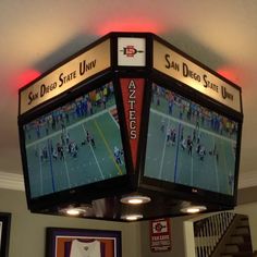 two large televisions mounted to the ceiling in a sports game room with lights on