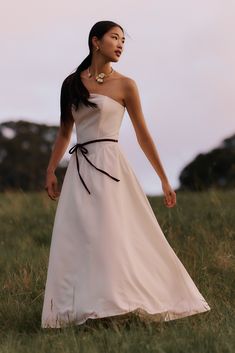 a woman in a white dress is walking through the grass with her hand on her hip