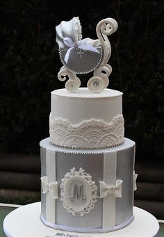 a three tiered wedding cake decorated with white and silver ribbons, bows and a baby carriage on top