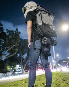 a person with a backpack and skateboard standing in the grass at night, looking down