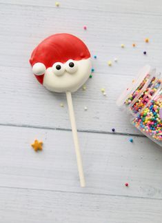 a santa face lollipop with sprinkles on it next to a container of candy