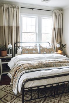 a bed sitting under a window in a bedroom next to a night stand and lamp