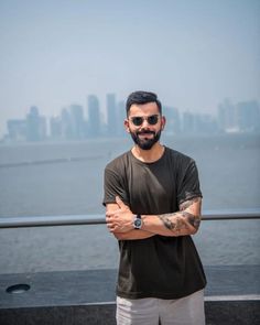 a man standing with his arms crossed in front of the ocean and city skyline behind him