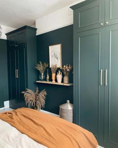 a bedroom with green painted walls and white bedding in the foreground is a wooden shelf filled with potted plants