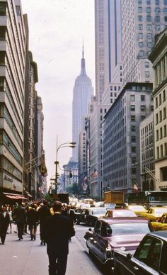 people are walking down the street in front of tall buildings and skyscrapers on a cloudy day