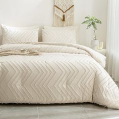 a bed with white comforter and pillows in a room next to a potted plant