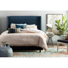 a bed with blue headboard and pillows on top of it in a bedroom next to a chair