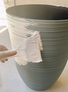 a person using a paint brush to paint a large gray vase with white stripes on it