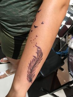 a woman with a tattoo on her arm has a feather and birds flying in the sky