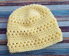 a yellow crocheted hat sitting on top of a wooden table next to a blue and white striped wall