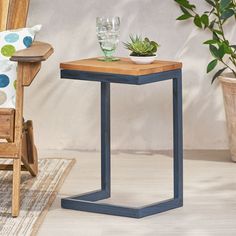 a wooden table sitting next to a chair with a plant on it and two glasses