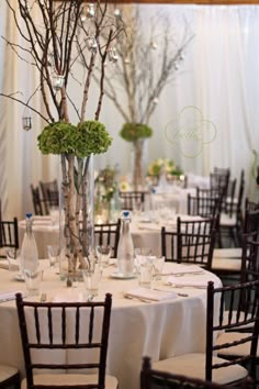 the tables are set with white linens and tall centerpieces filled with greenery