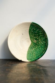 a green and white bowl sitting on top of a wooden table next to a wall