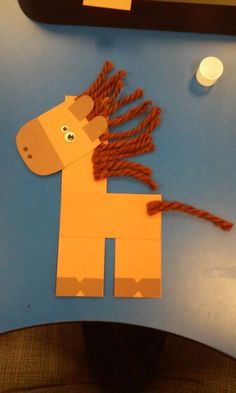 a horse made out of construction paper sitting on top of a blue table next to a cell phone