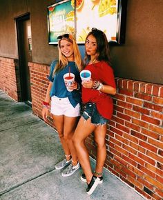 two young women standing next to each other near a brick wall and eating ice cream