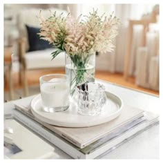 a glass vase filled with flowers sitting on top of a white plate next to a candle