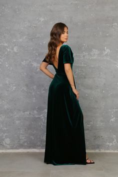 a woman in a green velvet dress standing against a concrete wall with her back to the camera