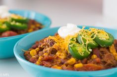 two blue bowls filled with chili and cheese on top of a white table next to each other