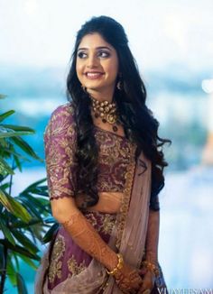 a woman in a purple and gold sari posing for the camera with her hands on her hips