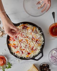 someone adding cheese to a skillet with other ingredients on the table next to it