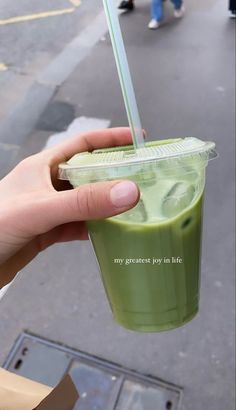 a hand holding a green smoothie in a plastic cup with a straw sticking out of it