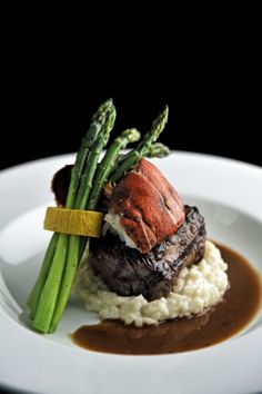 a white plate topped with meat and mashed potatoes covered in gravy next to asparagus