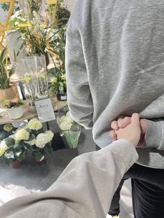 two people holding hands while standing next to each other in front of potted plants