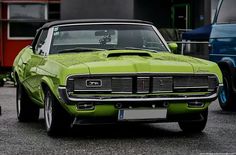 a green muscle car parked next to other cars