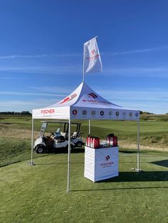 a golf cart parked under a white tent on the side of a green with a flag flying above it