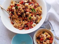 a bowl filled with pasta salad next to two bowls full of sauce and silverware