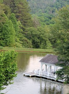 there is a white gazebo on the water in the woods with trees around it