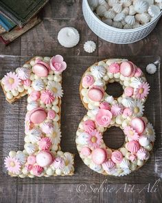 the number eighteen is decorated with pink and white icing, surrounded by seashells