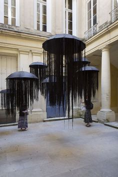 two people with umbrellas standing in front of a large sculpture that looks like it is suspended from the ceiling