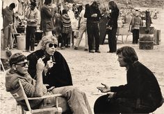 two women sitting on chairs talking to each other in front of a group of people