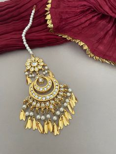 A bridal, kundan tika as part of your wedding jewelry you'll love! Shimmering kundan stones encrust the setting of this pretty maang tika with pipal patti drops strung with lustrous pearls.  Details: Length-8Inches Width-2.25 Inches All products are manufactured using traditional skills from our rich heritage of crafts.  The process of these crafts is essentially manual. Hence, any irregularities or variations are an inherent part of these handcrafting processes. White Cutdana Jhumkas For Wedding, Wedding White Cutdana Jhumkas, Kundan Necklace With Latkans, Kundan Bridal Sets With Gota Work For Wedding, Gold Chandbali Tikka With Zari Work, Bollywood Bridal Sets With Latkans For Festive, Bollywood Style Meenakari Dupatta For Wedding, Kundan Bridal Earrings With Tilla For Navratri, Kundan Jewelry For Wedding And Navratri